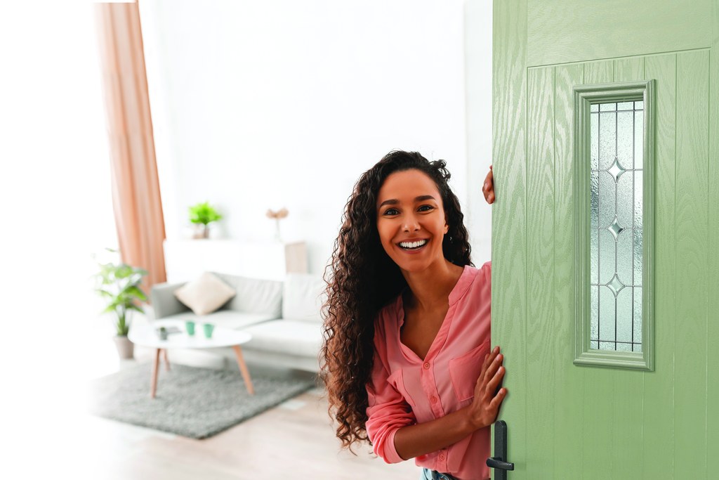 Woman standing beside a green entrance door with decorative glass